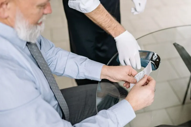 Diner checking his receipt while a waiter in white gloves holds the card machine