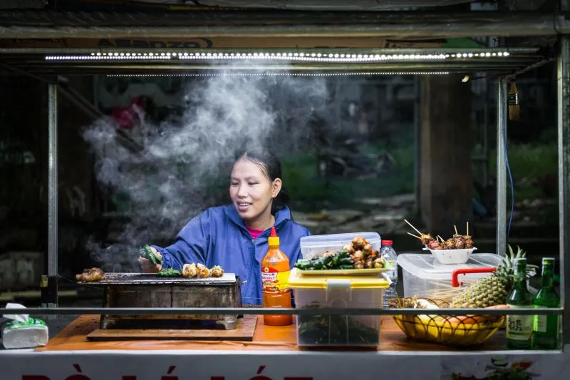 Street vendor grilling skewers behind the counter of her roadside stall in Vietnam