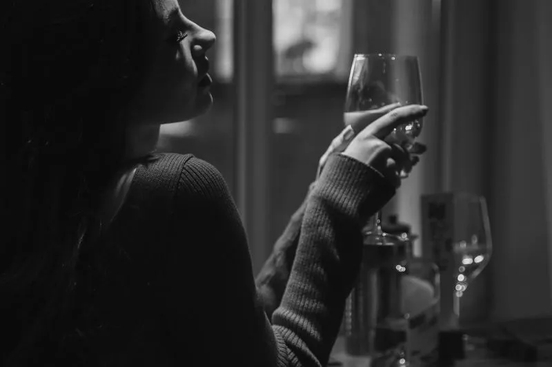 Woman sitting alone at a table with a glass of wine, in black and white