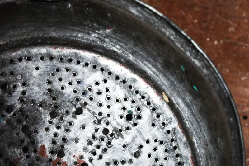 Close-up of the base of an old metal colander pierced with dozens of small holes, on a wooden table