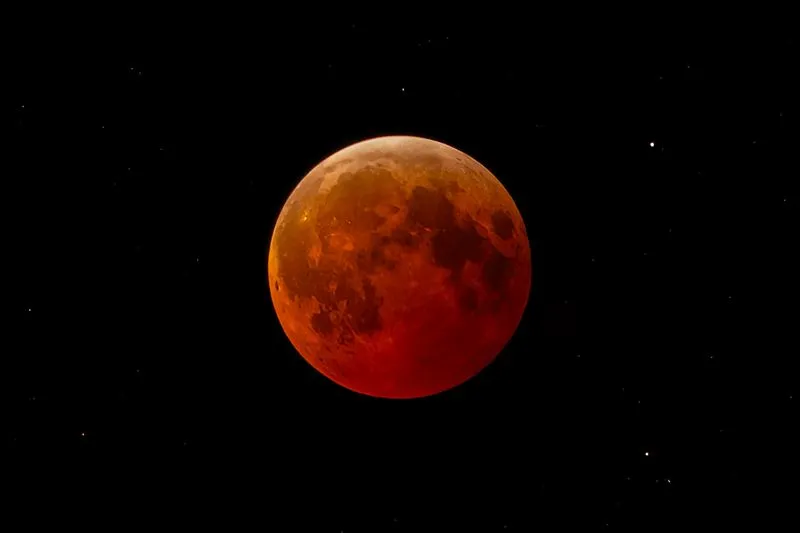 Copper-red full moon among a few stars in a black sky during a total lunar eclipse
