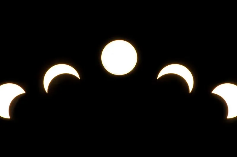 Composite of five views of a solar eclipse on a black background: the full solar disc in the centre, bitten into crescents on either side