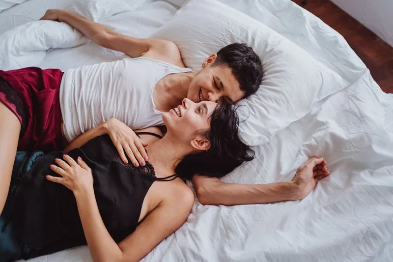 A couple lying on white sheets, laughing, faces close together