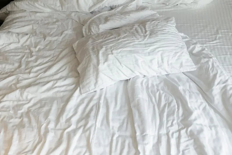 A white pillow on an unmade bed with crumpled sheets