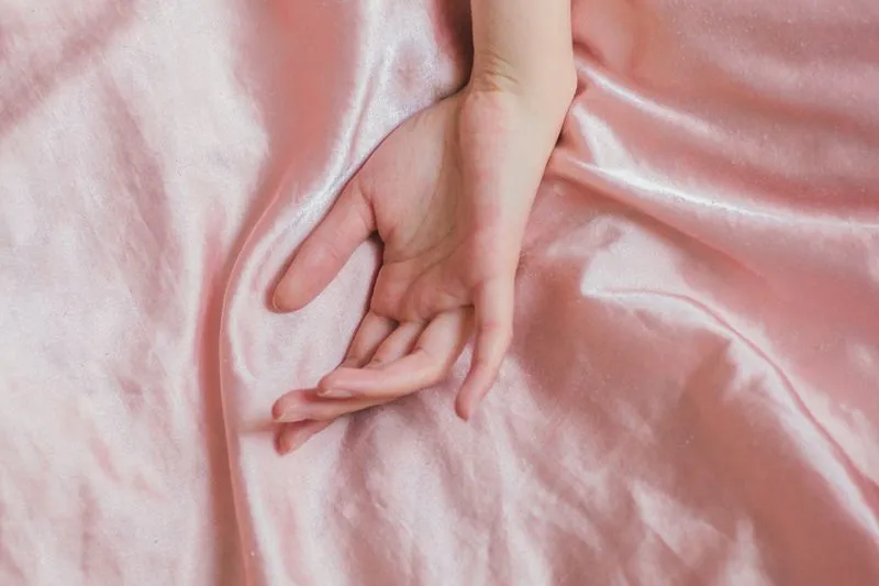 A woman's hand resting on a pink satin sheet