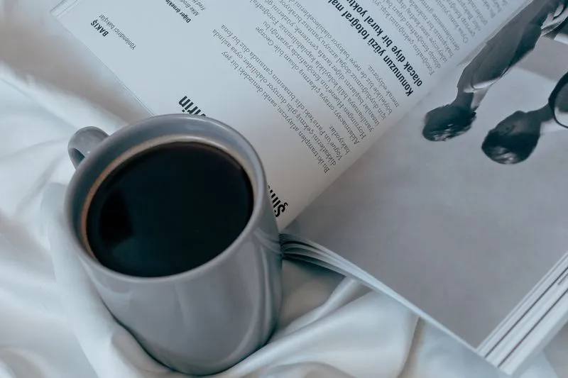 A cup of coffee resting on an open magazine among white sheets