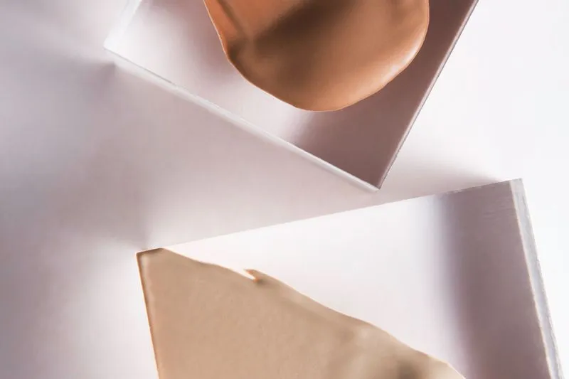 Two smears of liquid foundation, one beige and one caramel, spread on clear blocks