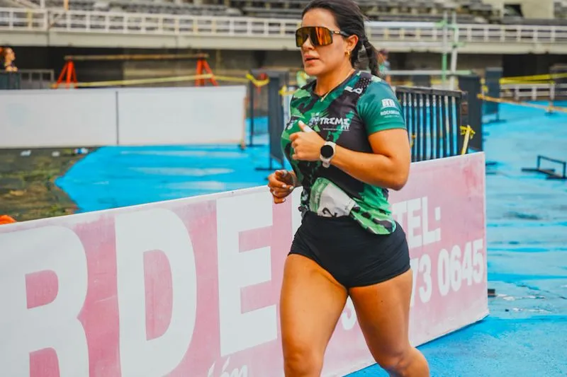 A runner on a stadium track in a green and black sports top, wearing large wraparound sports sunglasses