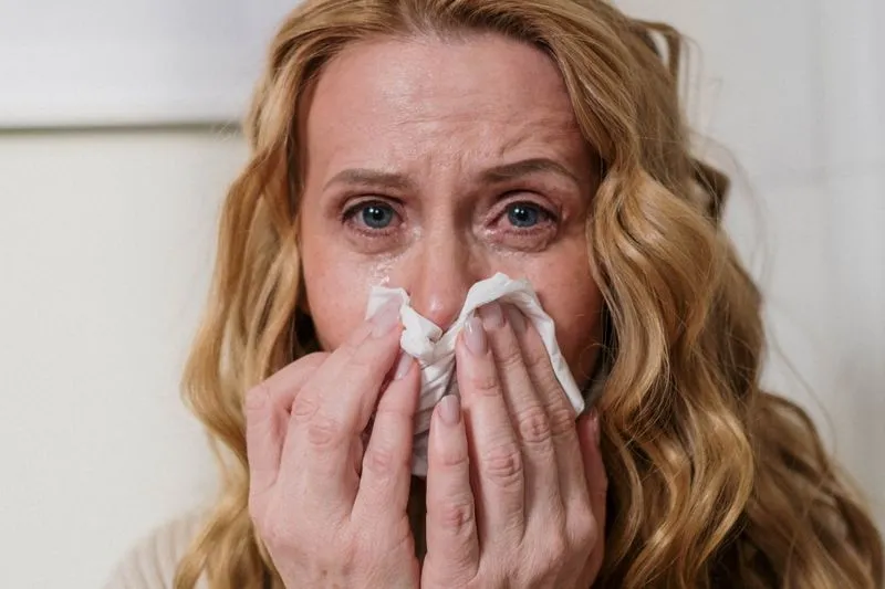 A woman with red, watery eyes pressing a paper tissue to her nose
