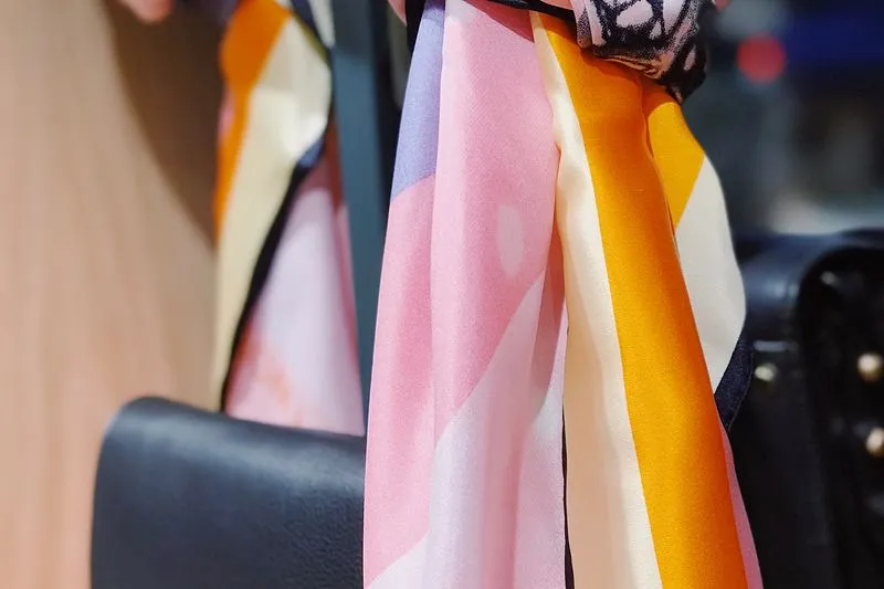 Silk scarf striped in pink, orange and cream, knotted on a black leather handbag