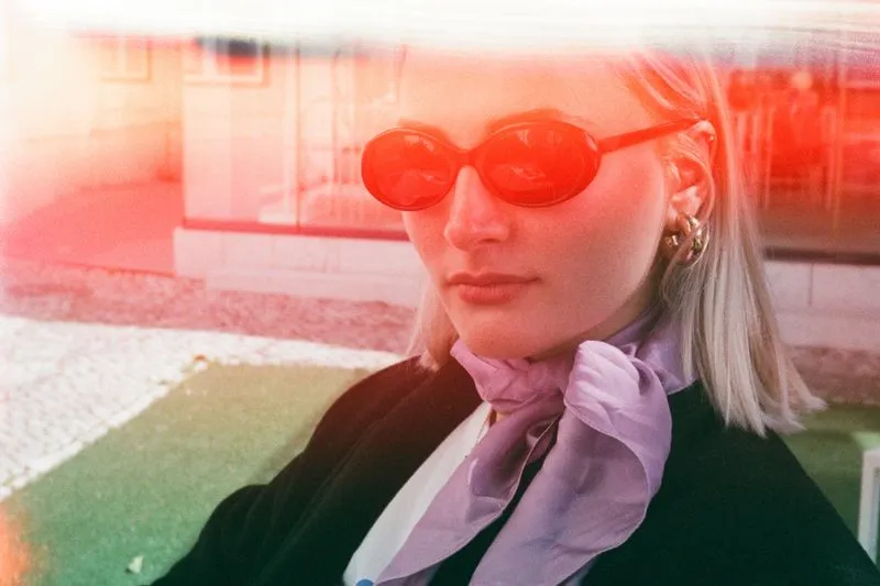Blonde woman in red sunglasses with a lilac silk scarf knotted at her neck over a black jacket