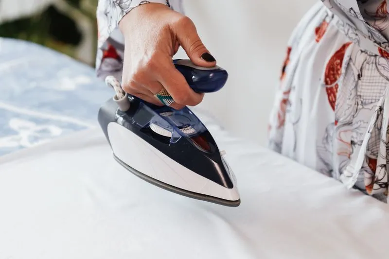 Hand running a steam iron over white fabric on an ironing board