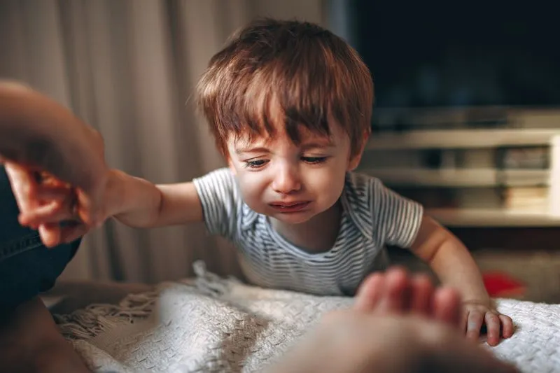 Little boy in tears, his mouth twisted with crying, reaching his arm out towards an adult's hand