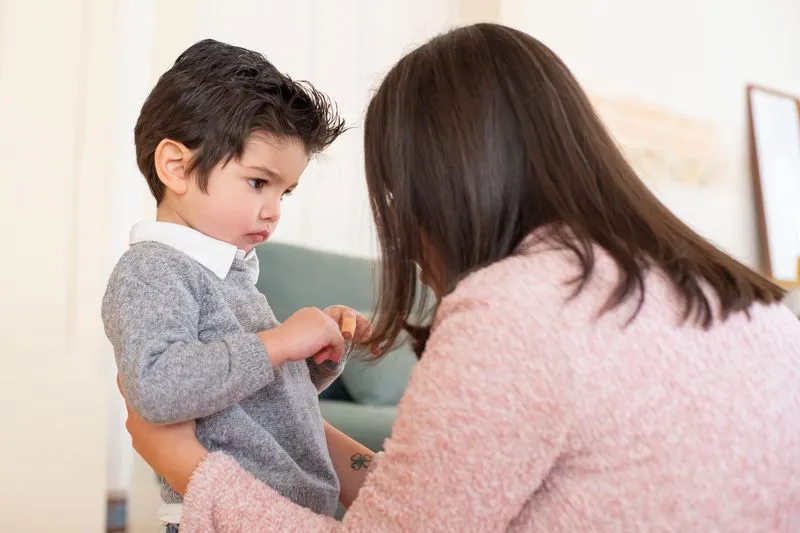 Mother leaning down to a little boy's height in a living room, speaking softly as he looks down