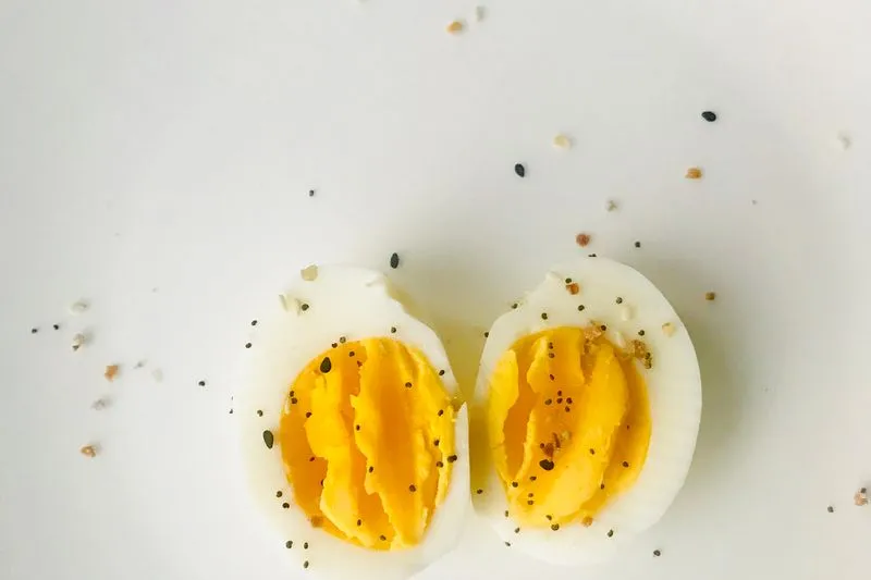 Two halves of a hard-boiled egg with a firm yolk, sprinkled with seeds, on a white background
