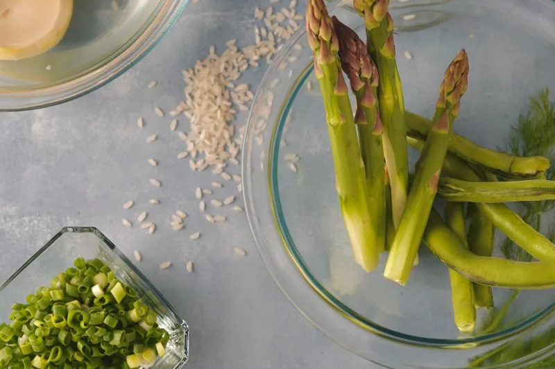 Green asparagus in a glass bowl and sliced spring onions in a small dish on a worktop