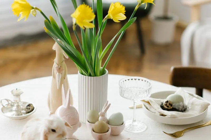 Easter table laid with a vase of daffodils, pastel eggs in egg cups, ceramic bunnies and a small rabbit in the foreground