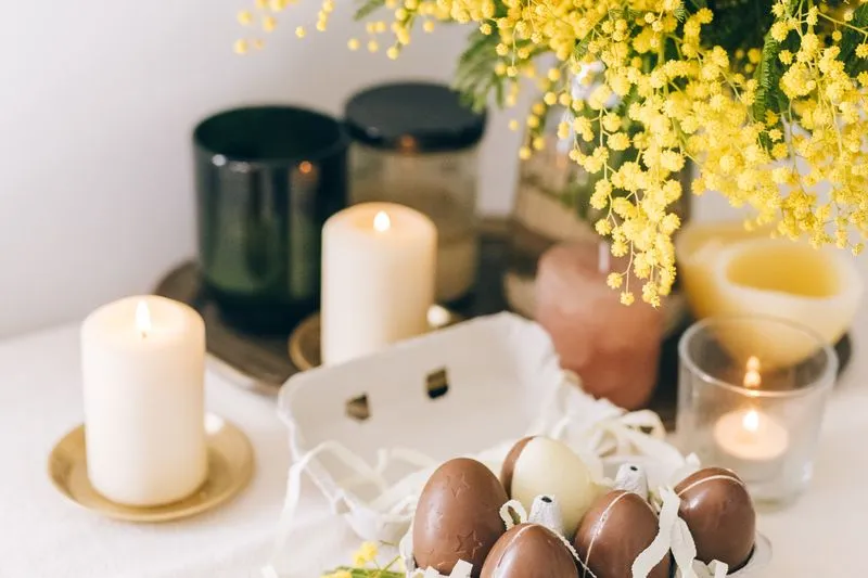 Sprigs of mimosa, lit candles and chocolate eggs in an egg box on a white tablecloth