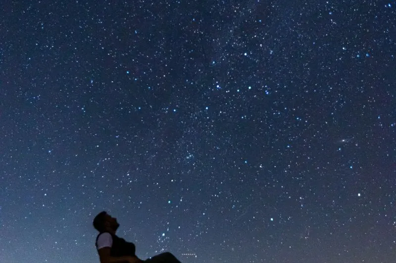 Silhouette of a man leaning back to gaze at a night sky thick with stars