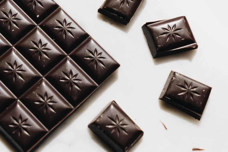A bar of dark chocolate and a few loose squares on a white surface
