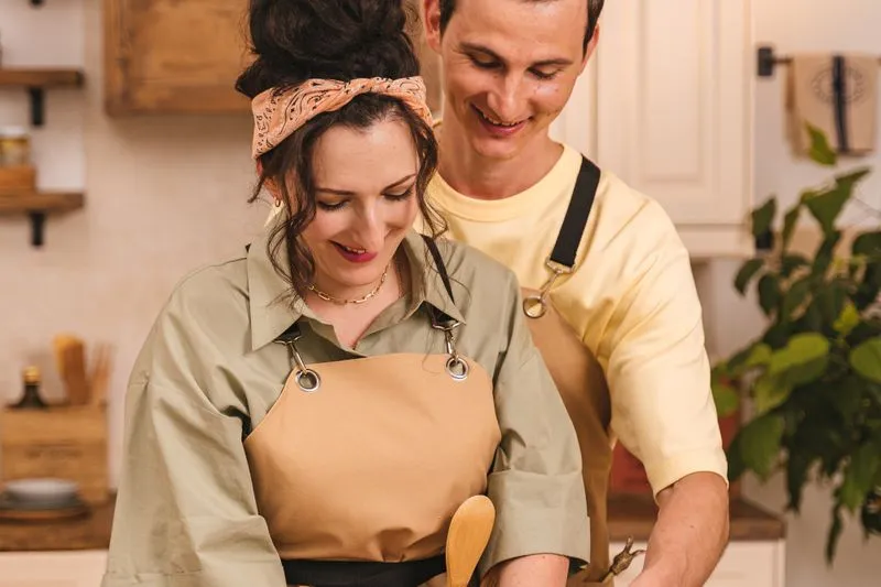 A smiling couple in aprons cooking side by side