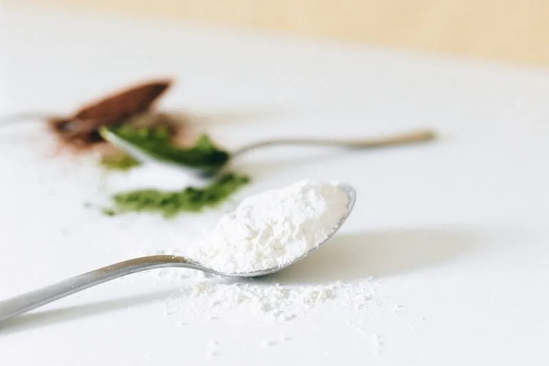 A spoonful of pale powder in the foreground, with green and brown powders behind