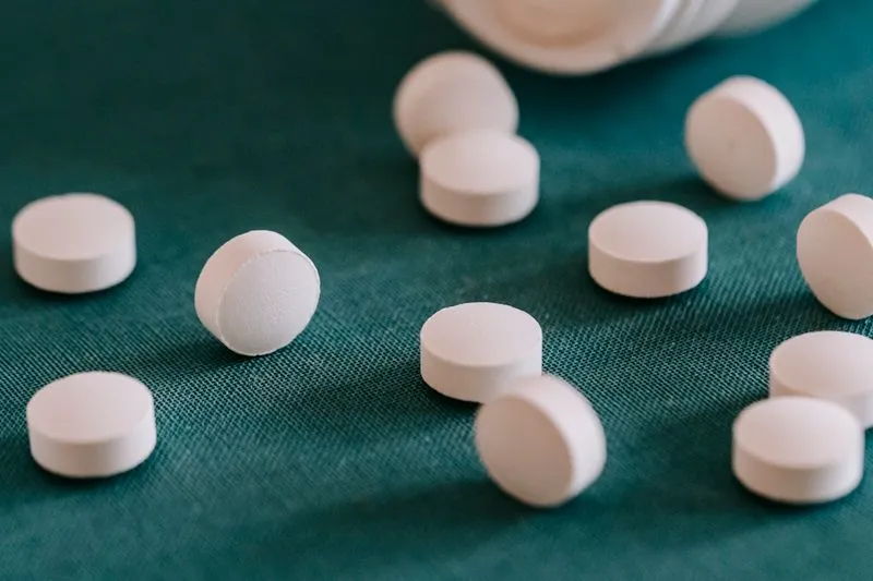 White tablets spilling from a bottle lying on its side on teal fabric