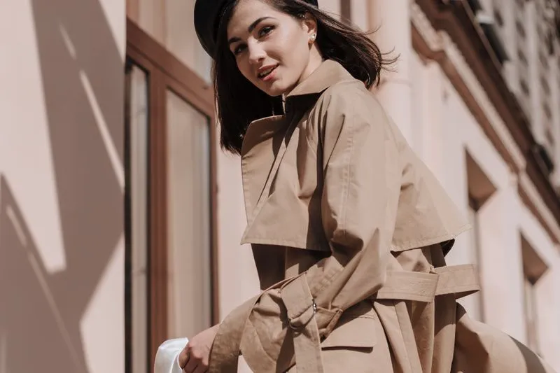 Woman in a black beret wearing a beige trench coat: storm cape over the shoulders, belt and metal buckle at the waist