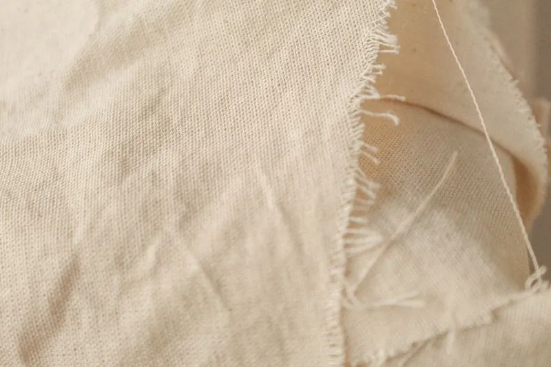 Close-up of unbleached cotton canvas with a frayed edge, its weave visible to the naked eye