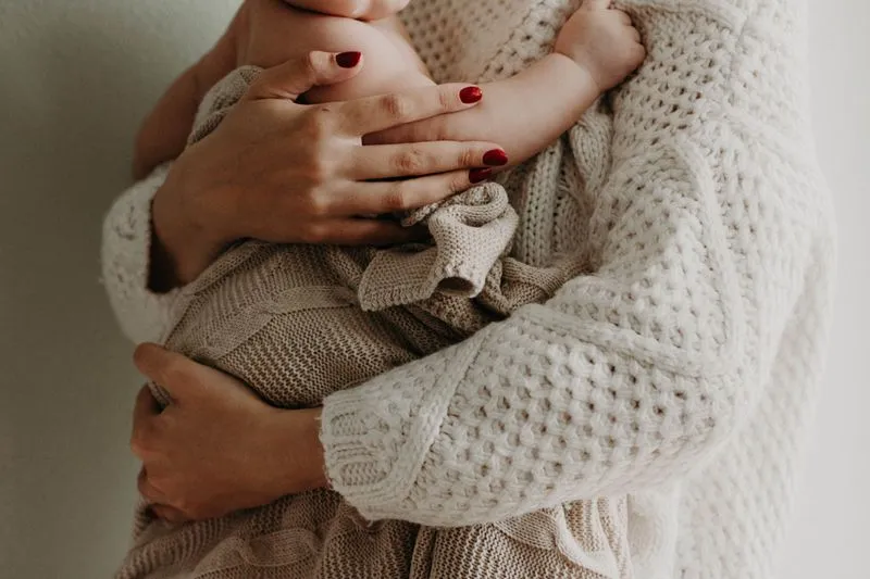 Mother holding her baby close, wrapped in a knitted blanket