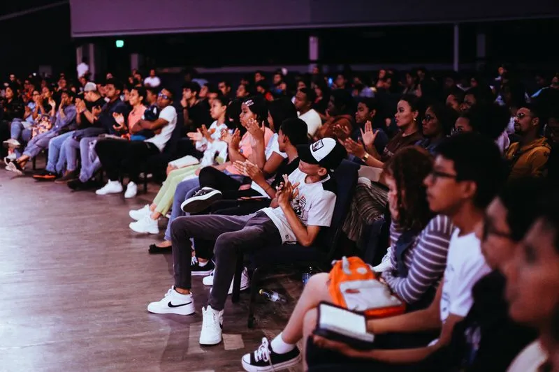 Rows of young seated spectators applauding in a dimly lit hall