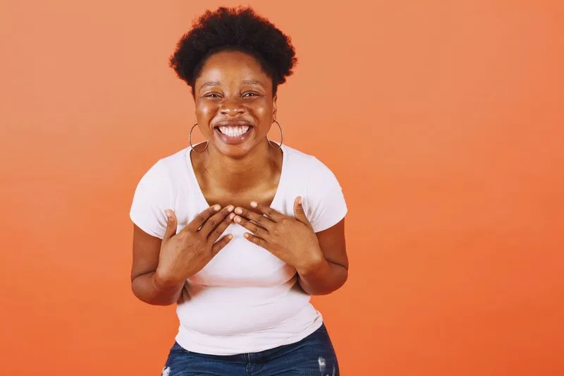 Laughing young woman in a plain white T-shirt and jeans against an orange backdrop