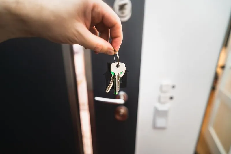 Hand holding a bunch of keys on a house-shaped key ring in front of an open front door