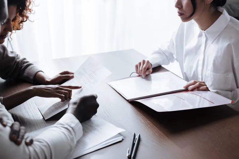 Couple sitting across a table from an adviser in a white shirt, documents and an open folder between them