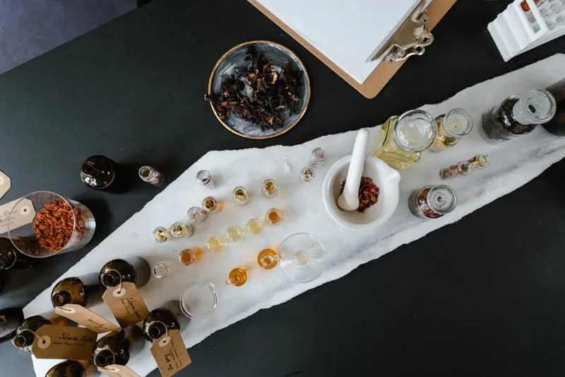 Overhead view of a perfume workshop: essence vials, labelled bottles, a mortar and dried petals