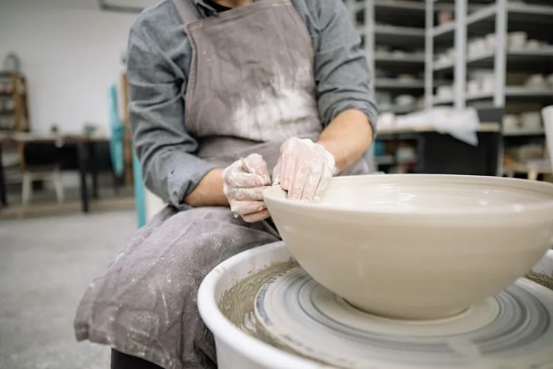 Clay-covered hands shaping a large bowl on a potter's wheel in a ceramics studio