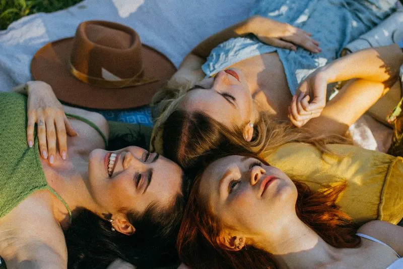 Three young women lying head to head on a blanket in the grass, in the late-afternoon sun