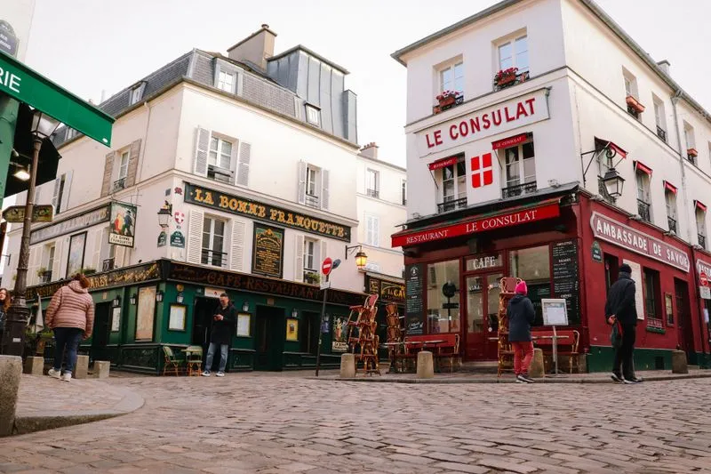 Cobbled Montmartre street corner with the red-fronted Le Consulat restaurant and the green-fronted La Bonne Franquette