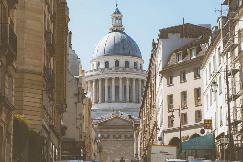 Latin Quarter street lined with stone apartment buildings, the dome of the Panthéon at the end under a blue sky