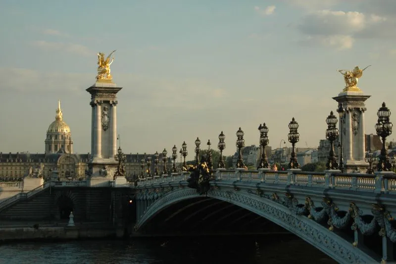 Pont Alexandre III in Paris with its ornate lamp posts and gilded statues, the dome of Les Invalides behind, the Seine in the foreground in late-afternoon light