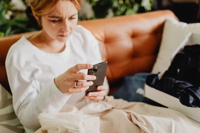 Woman in a white jumper sitting on a leather sofa, eyes fixed on her smartphone screen