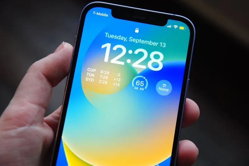 Hand holding an iPhone showing its lock screen, with the time and widgets