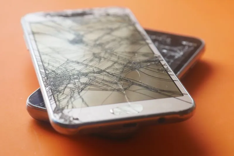 Two smartphones with shattered screens stacked on an orange surface