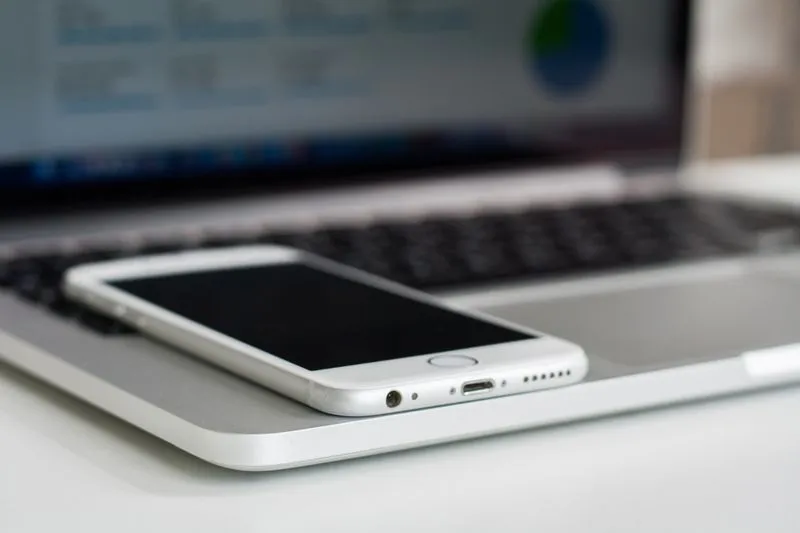 White iPhone resting on the palm rest of an open laptop