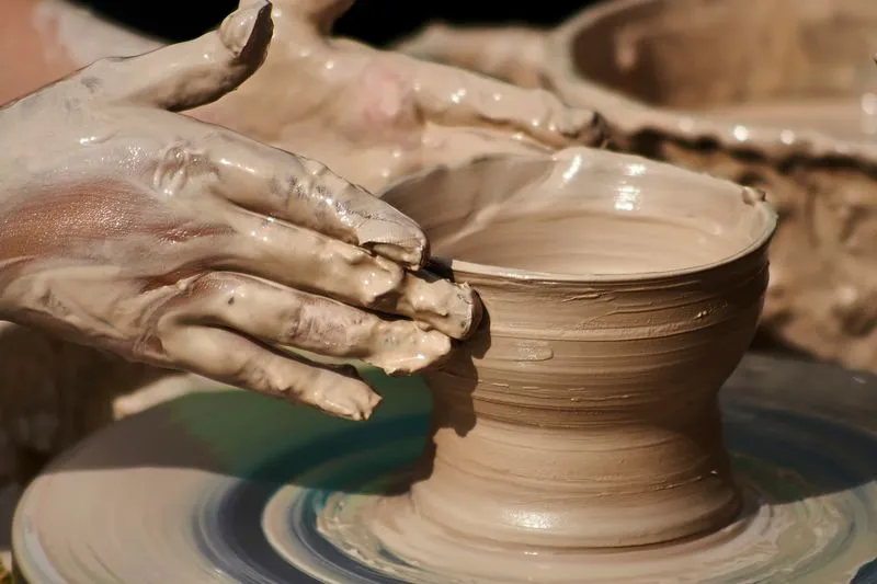 Clay-covered hands raising a pot on a potter's wheel