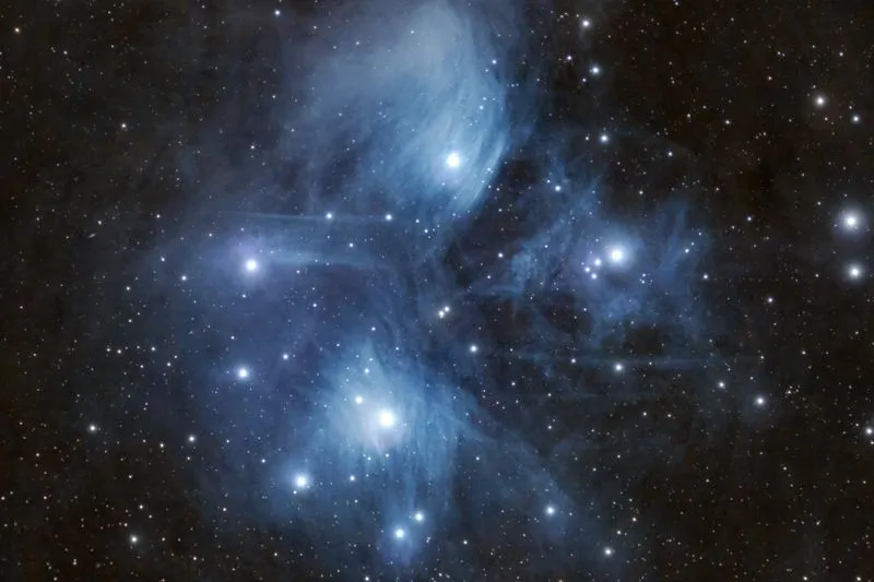 The Pleiades, a cluster of blue stars wrapped in a veil of nebulosity, against a starry sky