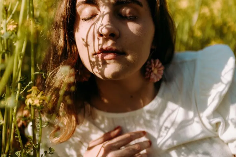 Young woman lying in tall grass with her eyes closed, flower shadows falling across her face in the sun