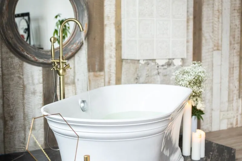 White bathtub filling under a brass tap, with candles and a bunch of gypsophila beside it
