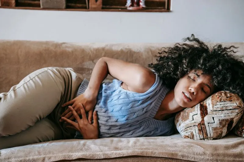 Woman lying on a sofa with her hands on her tummy, her face tense with pain