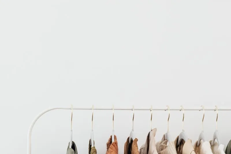 White clothes rail hung with neutral-toned pieces, from sage and rust to beige and cream